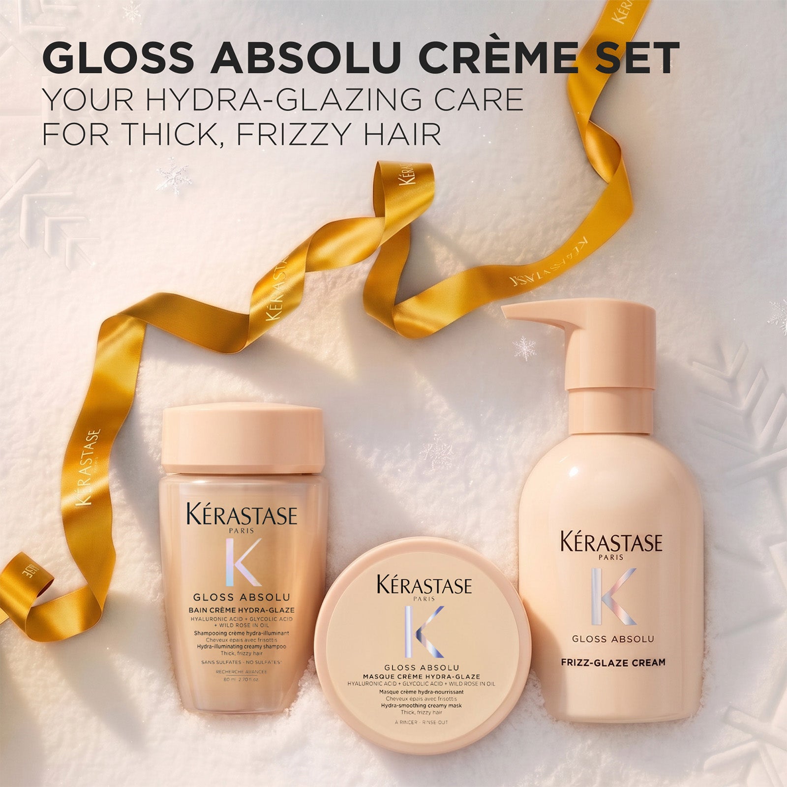 Image of Three Kérastase Gloss Absolu crème haircare products arranged on a white textured background with decorative text at the top and a gold ribbon. The set includes a jar, a round jar, and a pump bottle in a soft warm beige tone.