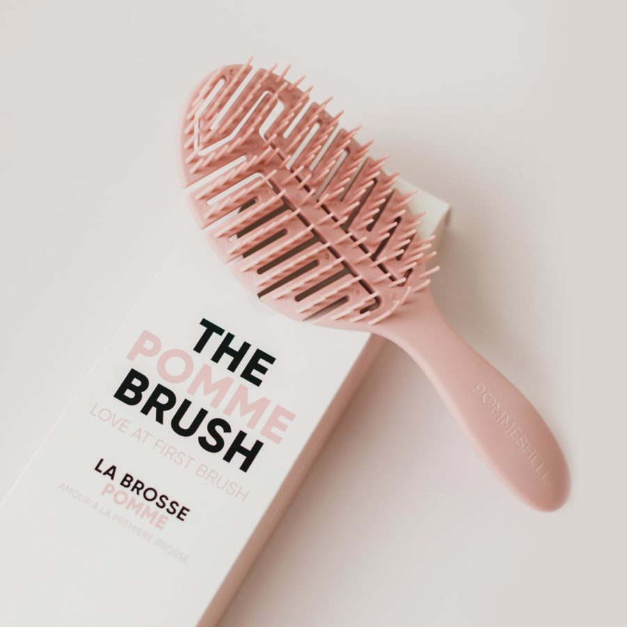 A pink hairbrush placed beside its packaging box on a pale background.