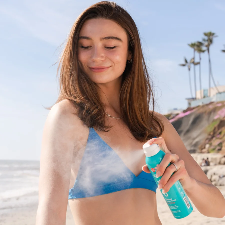 an image of a model smiling and spraying the guava mango sun screen on their arm.