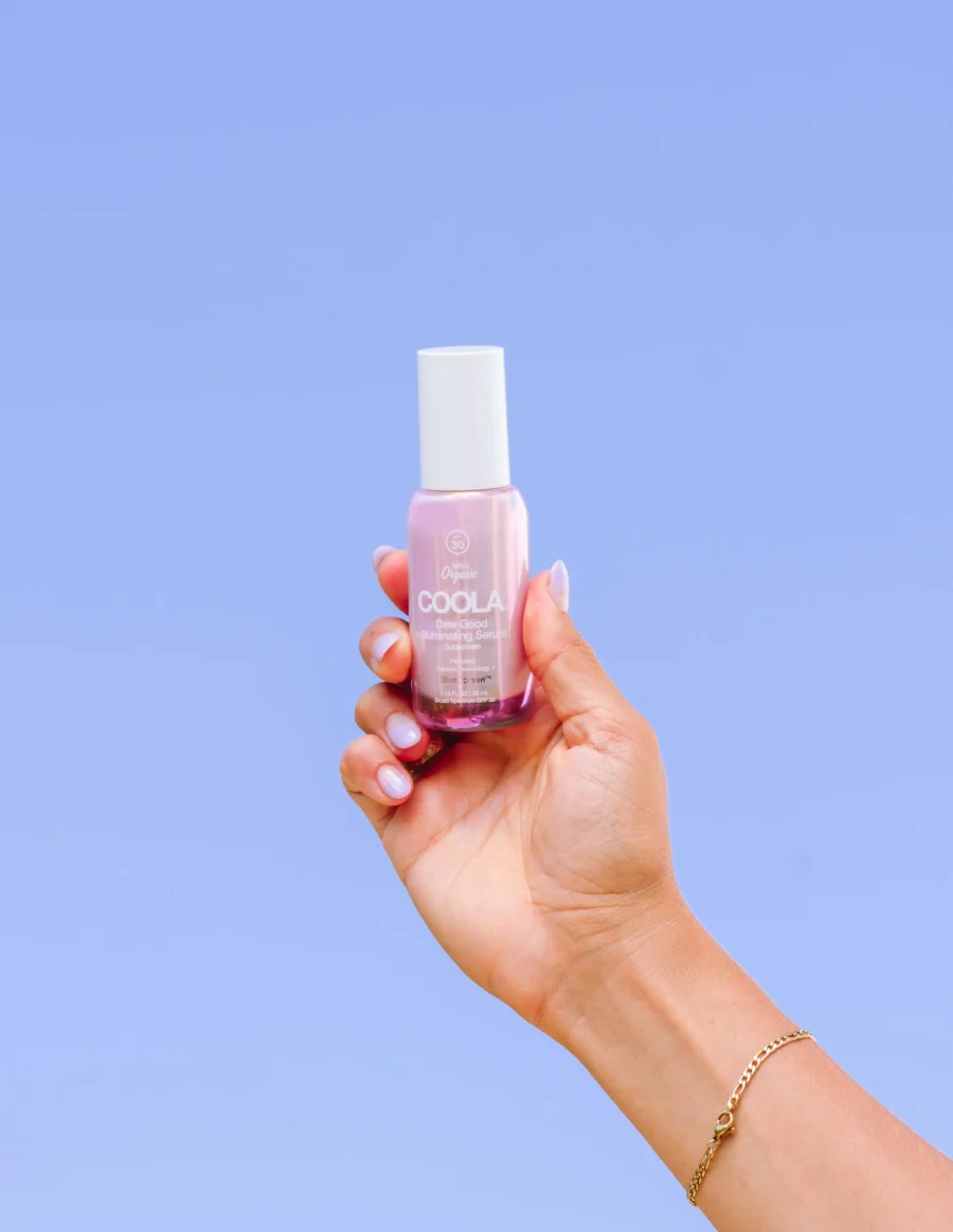 an image of the coola dew good serum in a hand against a blue background.